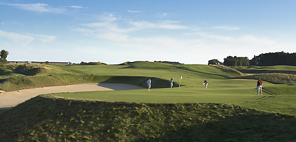 A landscape shot of one of Destination Kohler's golf courses includes a sand trap to the left and four golfers on the green to the right