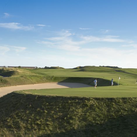 A landscape shot of one of Destination Kohler's golf courses includes a sand trap to the left and four golfers on the green to the right