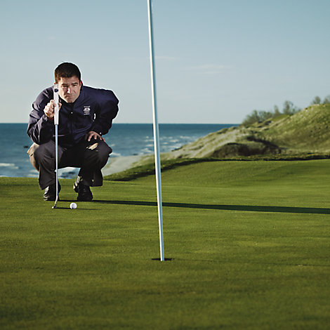 Mike O'Reilley, golf operations manager for Destination Kohler, squats down on the golf course as he eyes up a put. He's wearing a Whistling Straits windbreaker.
