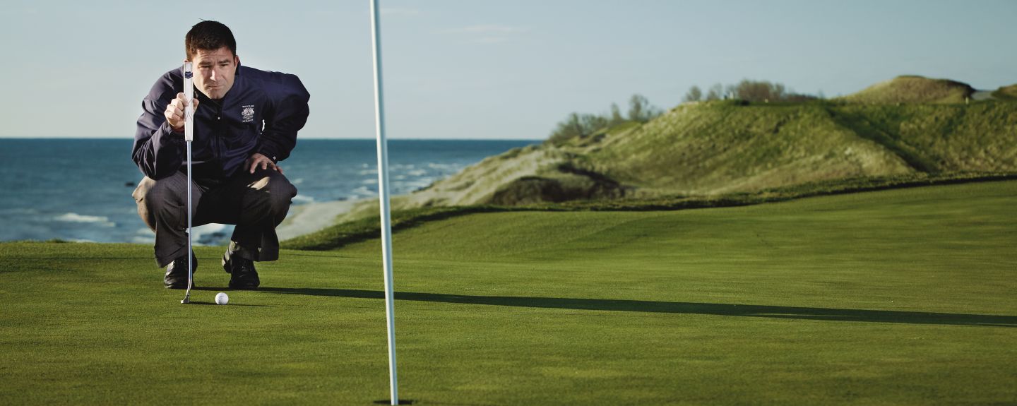 Mike O'Reilley, golf operations manager for Destination Kohler, squats down on the golf course as he eyes up a put. He's wearing a Whistling Straits windbreaker.