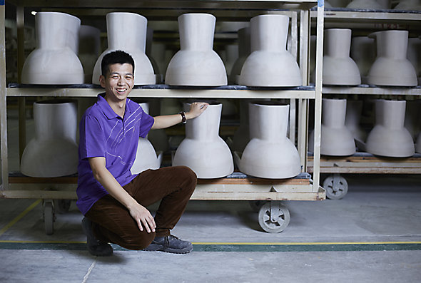 A Kohler Co. employee wearing a purple shirt kneels down to inspect racks of KOHLER toilets