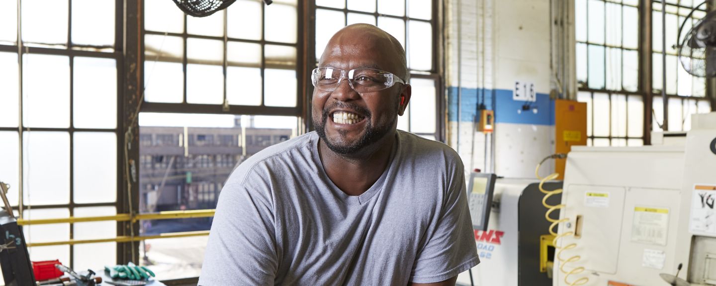 A man with a huge smile and safety glasses looks off to the distance