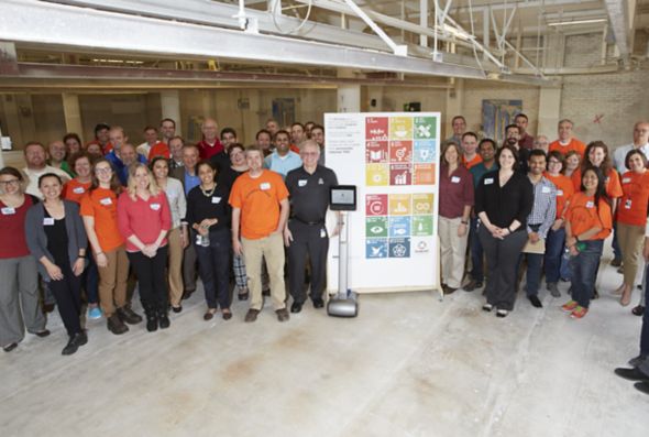 A large group of Kohler Co. employees stands by a sign with icons about sustainability