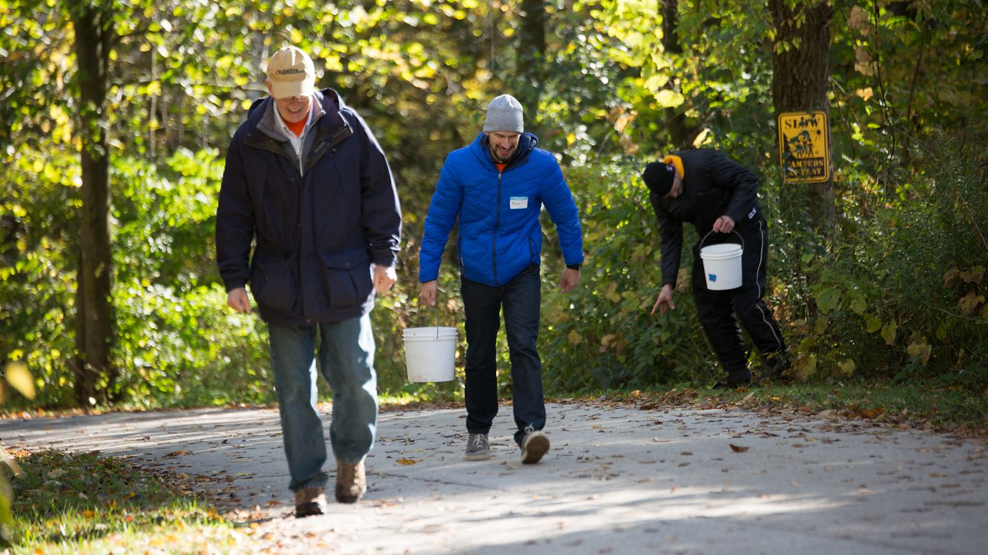 Three Kohler Co. employees walk on an outdoor path carrying five-gallon buckets