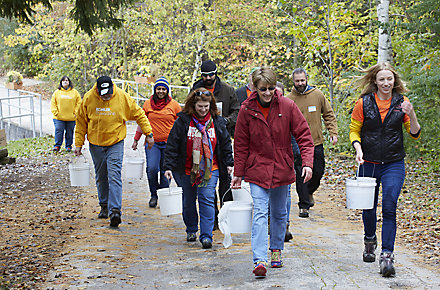 A group of Kohler employees walks through a path in the woods carrying 5-gallon buckets.