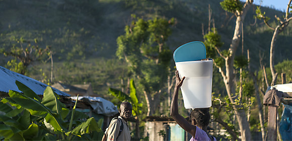 A woman carries a KOHLER® Clarity™ water filter on her head as a man looks on in Haiti
