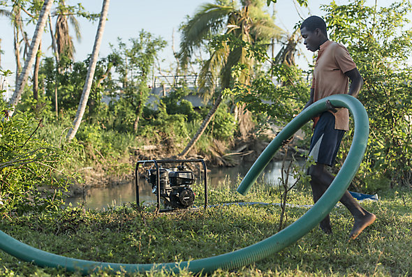 A man in Haiti hooks a big plastic pipe up to a KOHLER generator after Hurricane Matthew hit