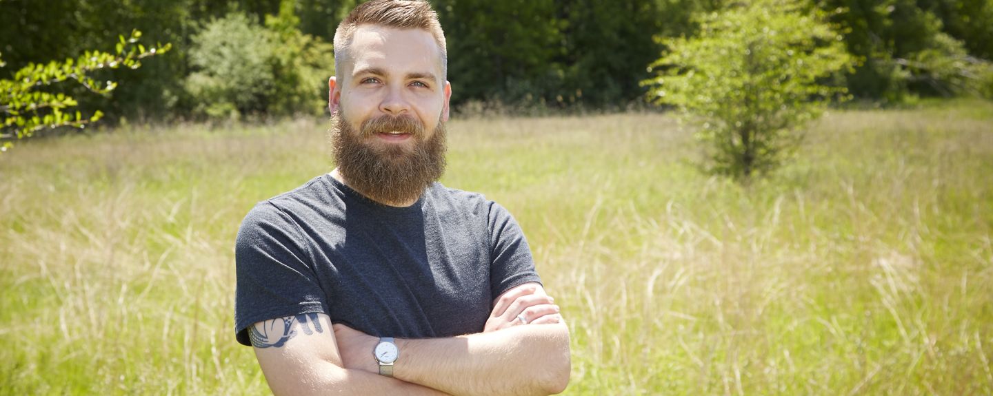Robert Dumville, Communications – Art Director, stands in a field with his arms crossed