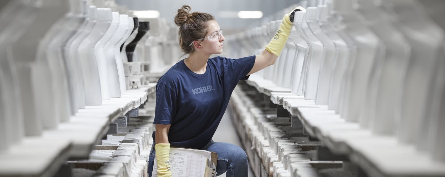 One of Kohler's employees kneels with a clipboard in front of a row of toilets she's inspecting