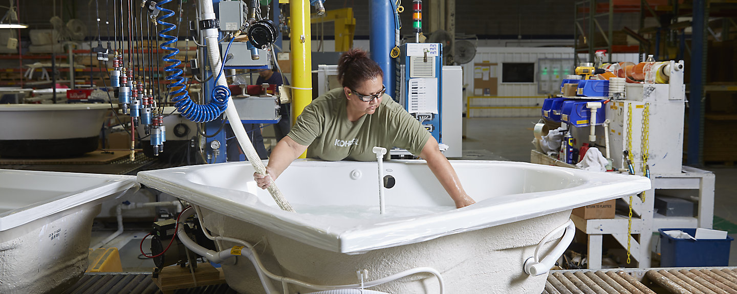 A woman wearing a KOHLER t-shirt fills water into a large bath in a manufacturing facility