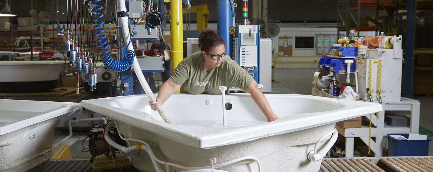 A woman wearing a KOHLER t-shirt fills water into a large bath in a manufacturing facility