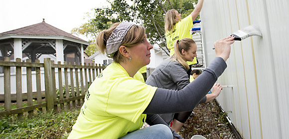 Three Kohler Co. employees paint a fence white as part of a volunteer experience