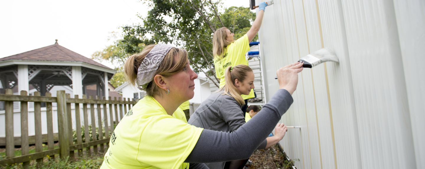 Three Kohler Co. employees paint a fence white as part of a volunteer experience