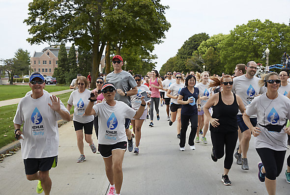 A large group of Kohler employee runs down the street in front of The American Club as part of the Run for Clarity