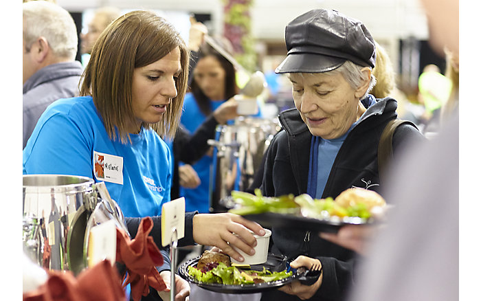 A woman with a blue t-shirt serves food to another woman at a community event