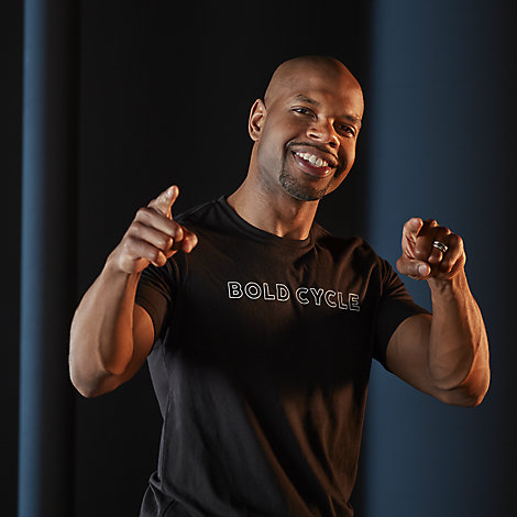 Rodney Ellison, an HR generalist at Kohler Co., looks at points at the camera. He's wearing a Bold Cycle t-shirt and standing in front of a dark blue backdrop