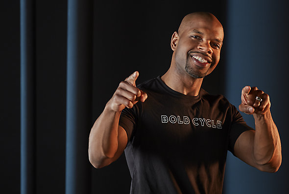 Rodney Ellison, an HR generalist at Kohler Co., looks and points at the camera. He's wearing a Bold Cycle t-shirt and standing in front of a dark blue backdrop