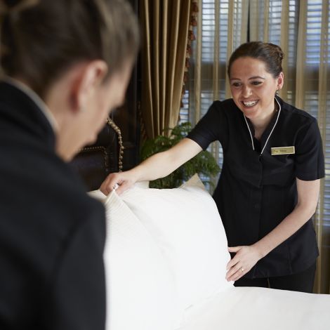 Two housekeepers in crisp, black dresses ensure the pillows are perfectly placed in a guest room at The American Club