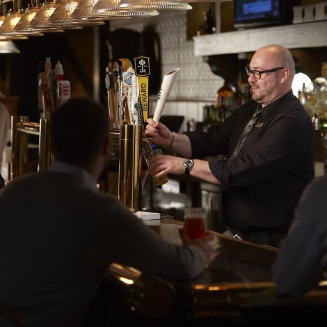 A bartender wearing a black shirt and tie pours a draft beer for guests sitting at the bar in front of him in Kohler, Wisconsin
