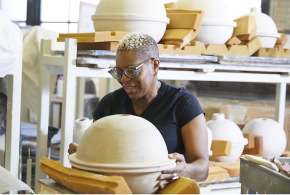 A woman sculpts a large clay piece of art in the Kohler Pottery, Iron and Brass Foundries, and Enamel Shop