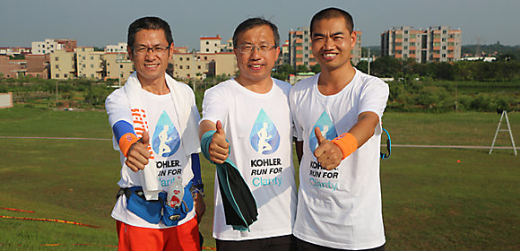 Three employees from the Kohler Co. plant in Foshan, China, stand outside together giving the thumbs-up symbol after completing a Kohler Run for Charity