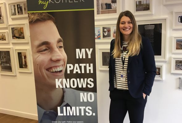 Cristina Bigica, Marketing and Communication – Buyer for Kohler Co., stands in front of a wall of framed artwork next to a sign.