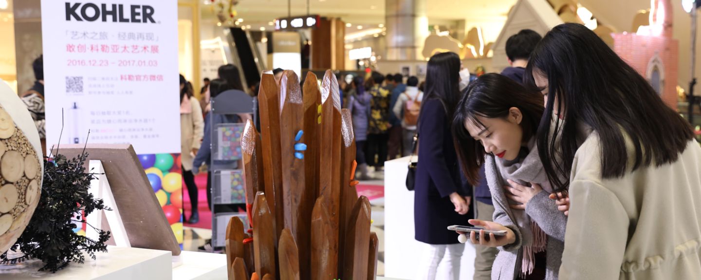Amidst a busy background, two women look at a sculpture.