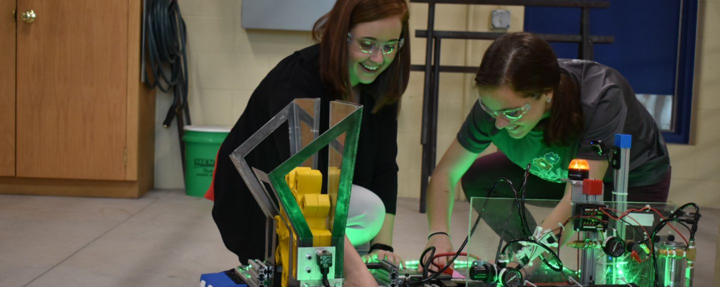 Engineer Megan Kennedy-Pierce and another Kohler Co. employee kneel on the floor by a robot they're helping build.