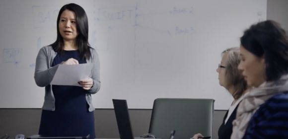 A woman who works in Finances at Kohler stands in front of a white board talking to two other employees