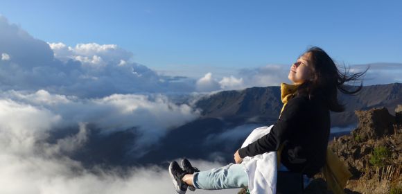 A Kohler intern sits at the edge of a cliff with a gorgeous view of mountains and clouds in the background