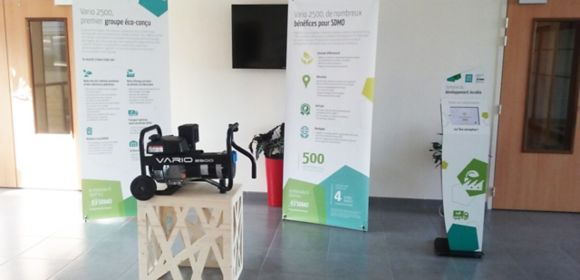 The portable Vario 2500 generator on a stand in front of signs explaining its benefits
