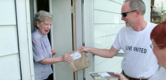 Two people, one in a Live United t-shirt, deliver food cooked by Destination Kohler chefs to a woman.