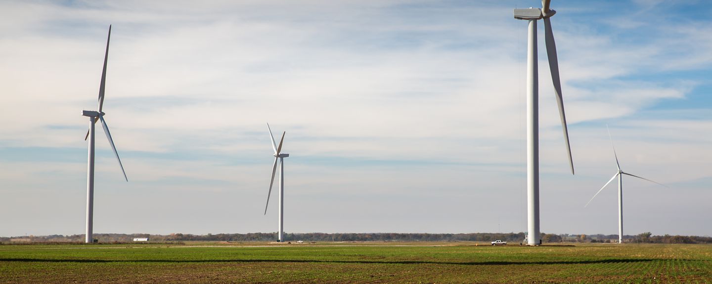 A broad landscape shot of windmills in farm fields with a truck driving by