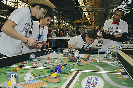 Three kids and an adult gather around a table during a LEGO Robotics competition