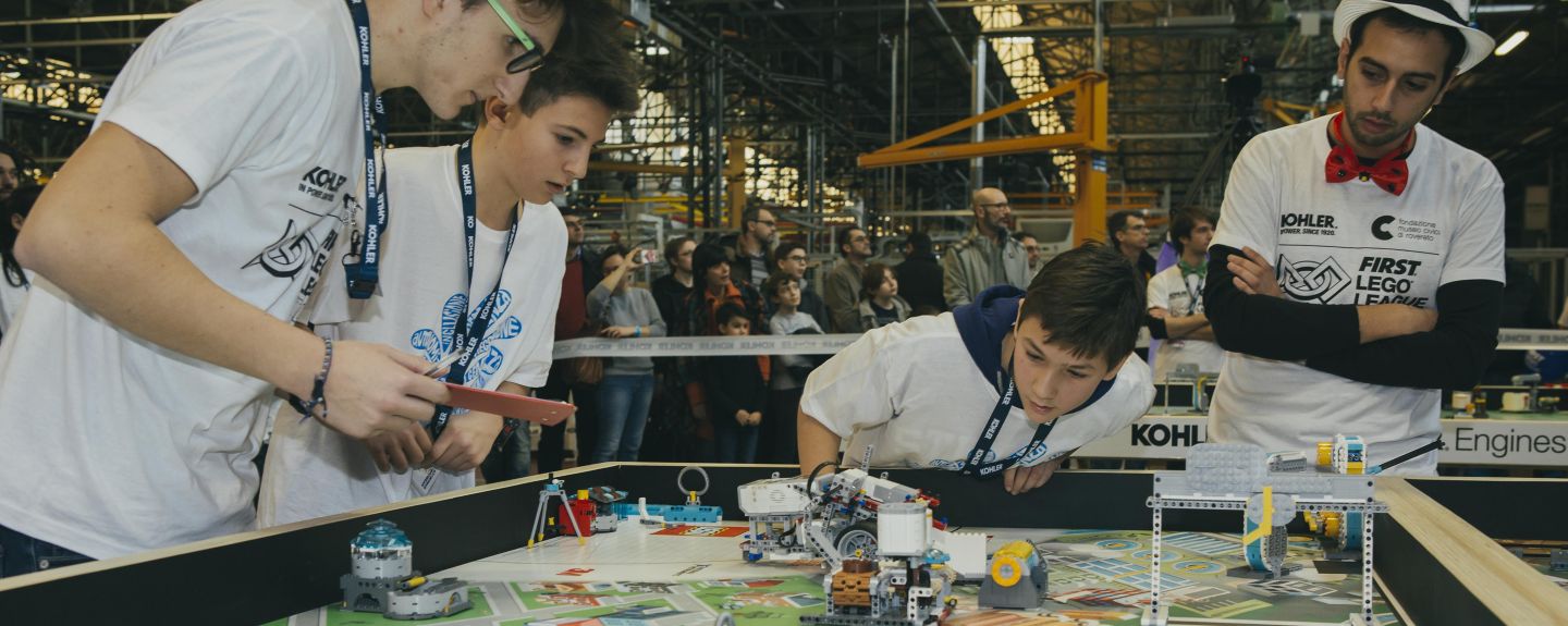 Three kids and an adult gather around a table during a LEGO Robotics competition