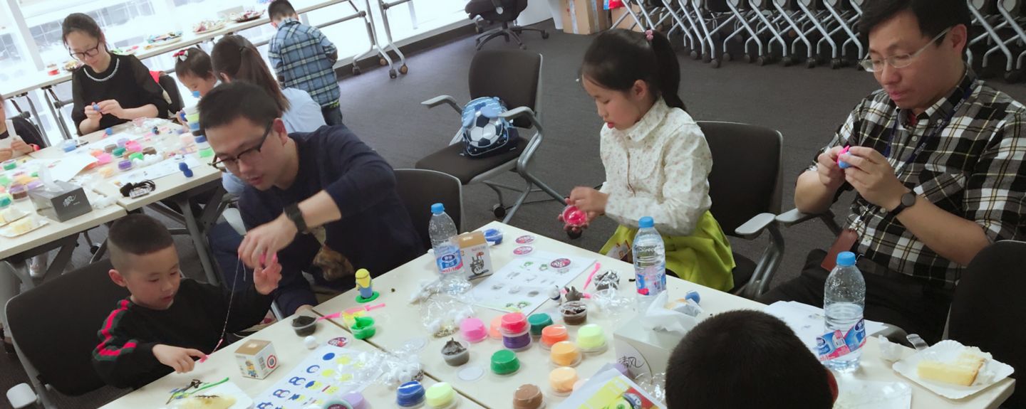 Kids and adults sit around tables loaded with art supplies.