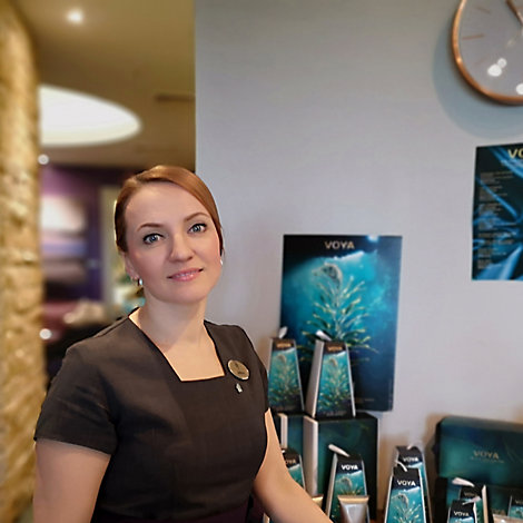 A woman wearing a black dress and name tag stands in the Kohler Water Spa at St Andrews, Scotland, with spa retail products in the background