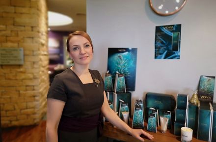 A woman wearing a black dress and name tag stands in the Kohler Water Spa at St Andrews, Scotland, with spa retail products in the background