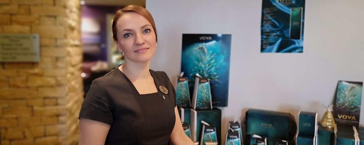A woman wearing a black dress and name tag stands in the Kohler Water Spa at St Andrews, Scotland.