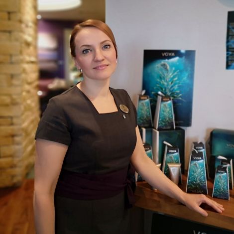 A woman wearing a black dress and name tag stands in the Kohler Water Spa at St Andrews, Scotland, with spa retail products in the background