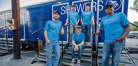 Five Kohler Co. employees in matching blue t-shirts pose in front of the KOHLER Relief Shower Trailer