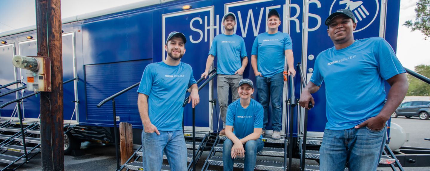 Five Kohler Co. employees in matching blue t-shirts pose in front of the KOHLER Relief Shower Trailer