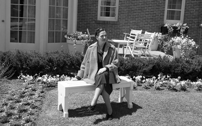 Ruth Kohler poses on a bench in front of a brick home in this black and white photo