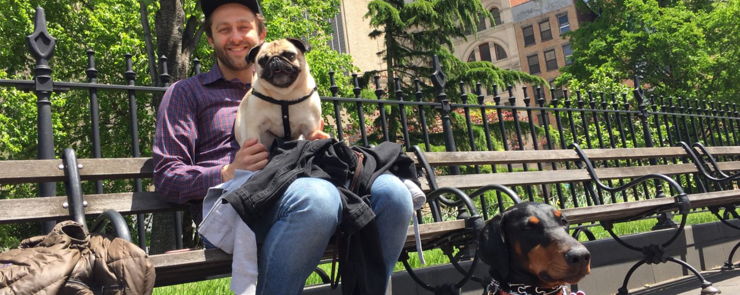Seth Stevens sits on a park bench with one dog on his lap and another in front of him