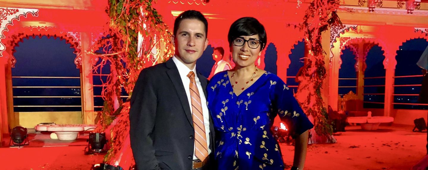 Romina Uceda stands with a man at a brightly lit and decorated open-air event space.
