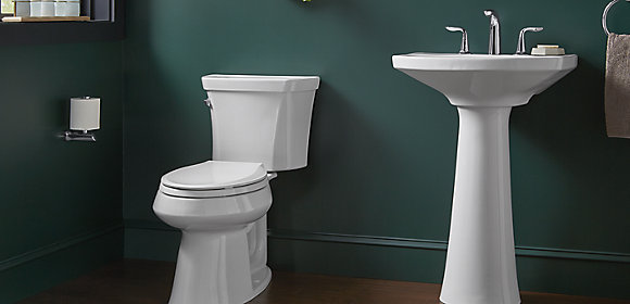 A KOHLER toilet and pedestal sink set against a dark green wall