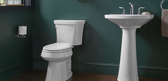 A KOHLER toilet and pedestal sink set against a dark green wall
