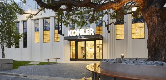 A photo taken from outside shows the front entrance to a LEED-certified KOHLER showroom. The interior is lighted and a KOHLER sign hangs by the front door