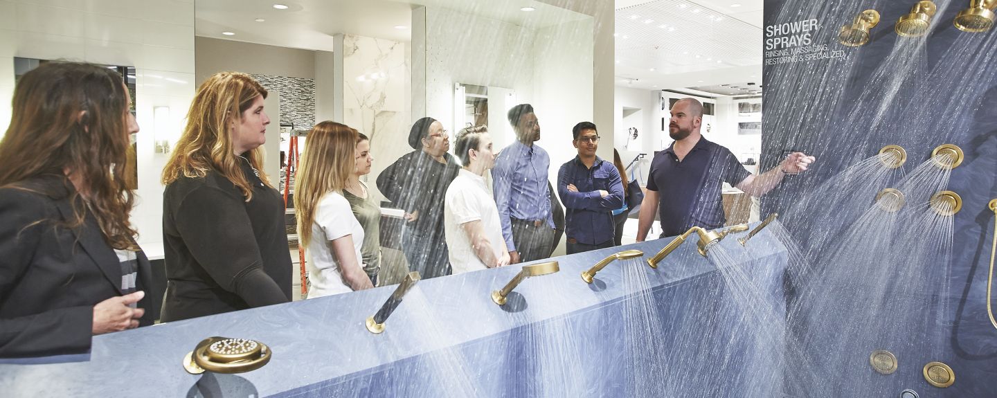 A group of employees looks at a working display of KOHLER showerheads, all spraying water