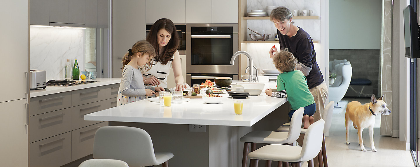 A family of four stands in a beautiful, modern kitchen with KOHLER faucets.
